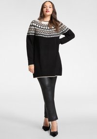 Czarny dziergany sweter z białym i kremowym wzorem na karczku, długimi rękawami i luźnym krojem, zestawiony z czarnymi spodniami ze sztucznej skóry i czarnymi szpilkami.