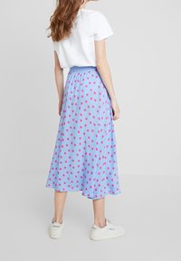 Gonna midi azzurro chiaro con pois rosa, vita elasticizzata e tessuto fluido, abbinata a una t-shirt bianca e sneakers bianche.