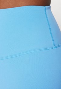 Svijetloplave tajice visokog struka napravljenih od glatkog, rastezljivog materijala. Sadrže ravne šavove duž šavova za dodatnu izdržljivost.