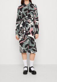 Košilové šaty vyrobené z lehké látky s barevným abstraktním vzorem listů v černé, zelené, bílé a růžové barvě. Obsahuje pásek.