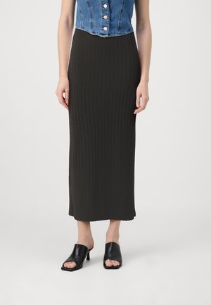 Black ribbed maxi skirt with a fitted design. Paired with open-toe black leather mules. Model wears a denim sleeveless top.