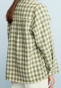 Green and beige checked flannel shirt with a rounded hem, buttoned cuffs, and a relaxed fit. Soft texture and casual design.
