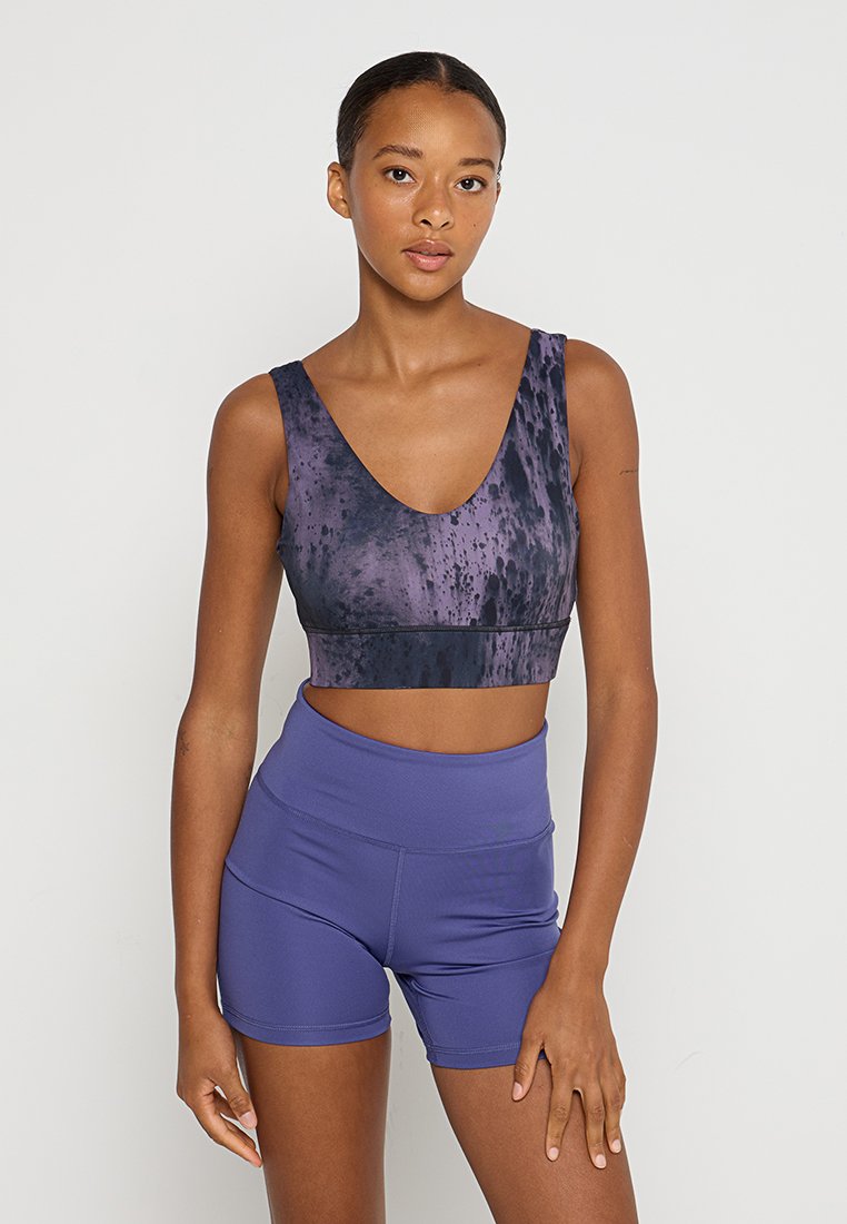 Seno di sport viola con design a scollo a V e motivo a schizzi, abbinato a pantaloni corti viola a vita alta. Tessuto dalla consistenza liscia.