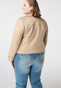 Tan faux suède jas met een kort design, voorzien van een klassieke kraag en gerolde manchetten, gecombineerd met mid-rise blauwe denim jeans.