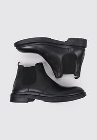 Botas Chelsea de cuero negro con paneles laterales elásticos, punta redonda y tacón bajo apilado. Textura suave y suela de goma resistente.