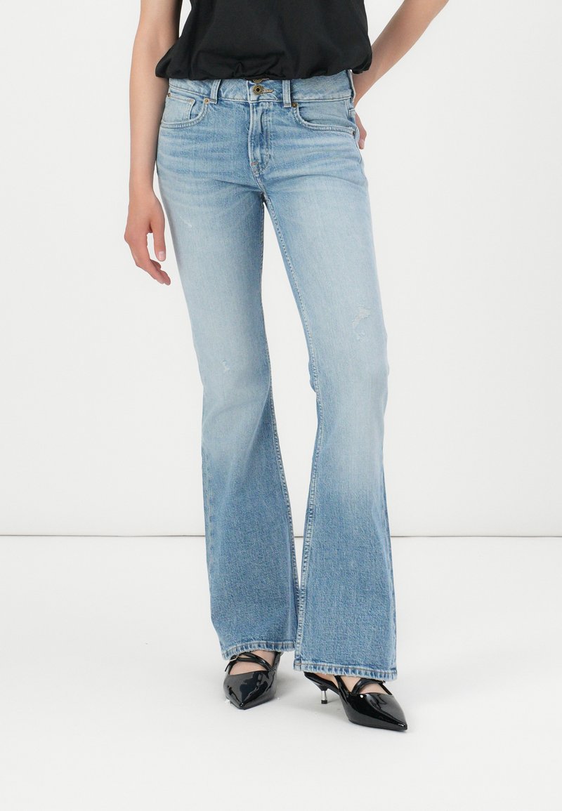 Light blue flared jeans made of denim, featuring a mid-rise waist, subtle distressing, and a slightly frayed hem. Paired with black heels.