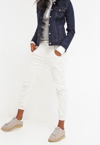 Joggers de algodón blancos con puños elásticos, combinados con una sudadera gris y una chaqueta de mezclilla oscura. Zapatillas de deporte gris claro con suela texturizada.