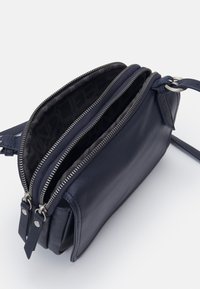 Navy kožená crossbody taška s dvojitými zipovými oddíly. Uvnitř má vzorované podšívku. Součástí je nastavitelný popruh a kovové akcenty.