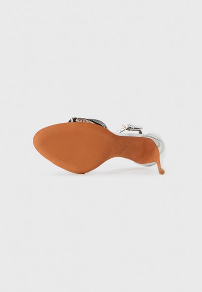 Pantof high heel cu degetele descoperite, având un superior argintiu, o talpă din cauciuc bej și o bandă distinctivă texturată de culoare neagră cu accente metalice.