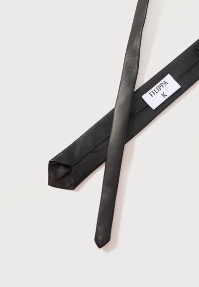 Cravate en cuir noir avec une étiquette blanche portant l'inscription "FILIPPA K" sur la face intérieure, présentée sur un fond clair.