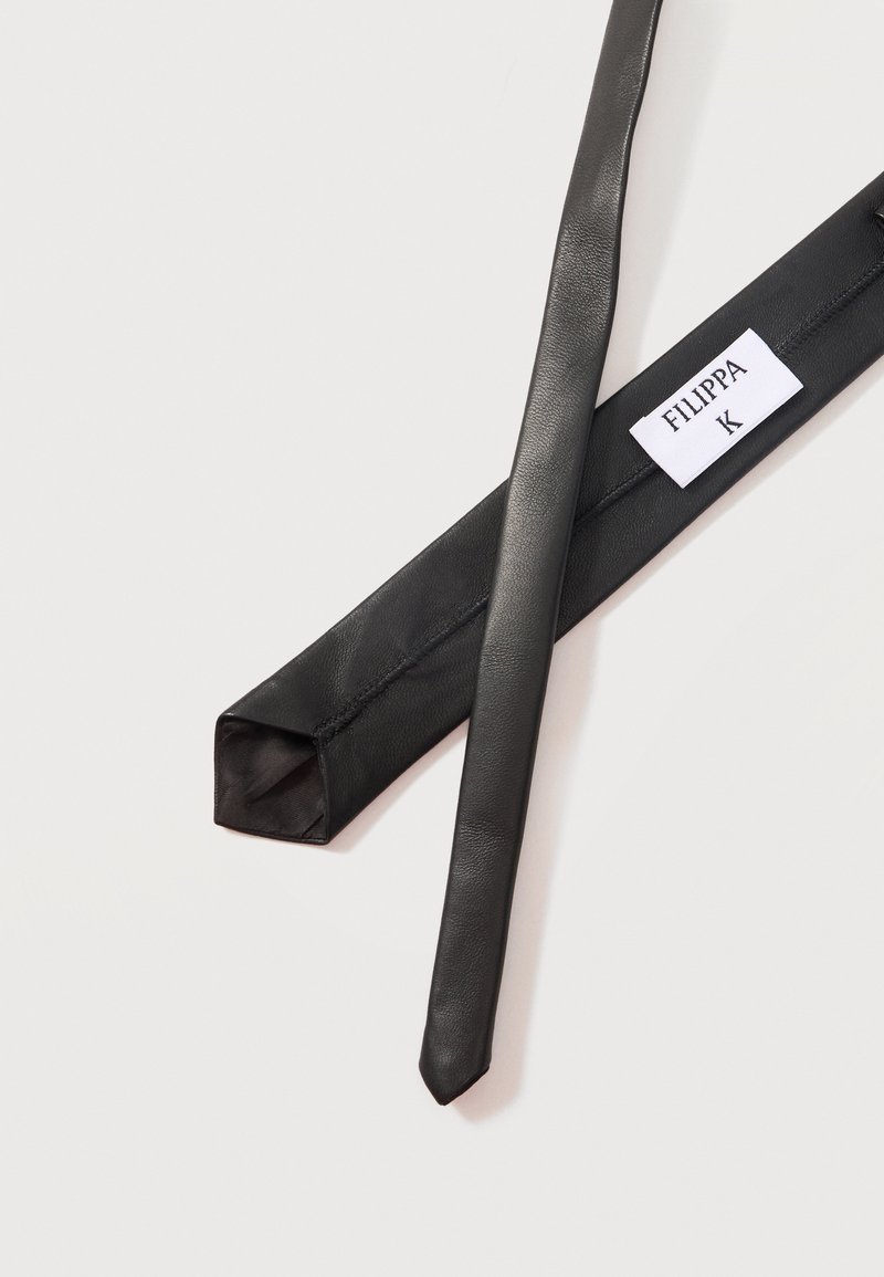 Schwarze Lederkrawatte mit einem weißen Etikett mit der Aufschrift "FILIPPA K" auf der Innenseite, dargestellt auf hellem Hintergrund.