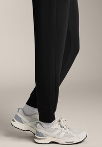 Čierne zúžené teplákové nohavice so bočnými švami, v kombinácii s bielymi a svetlomodrými športovými topánkami, ktoré majú sieťovinové panely a šnúrky.