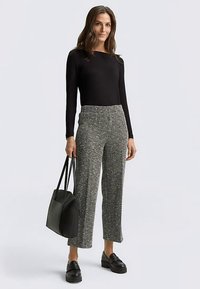 Haut noir à manches longues, pantalon gris texturé à jambes larges avec un motif pied-de-poule. Sac à épaule noir et chaussures noires épaisses.