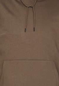 Felpa marrone realizzata in materiale morbido, con tasca a marsupio, cappuccio con cordino e una sottile texture. Aglet neri sui cordini.