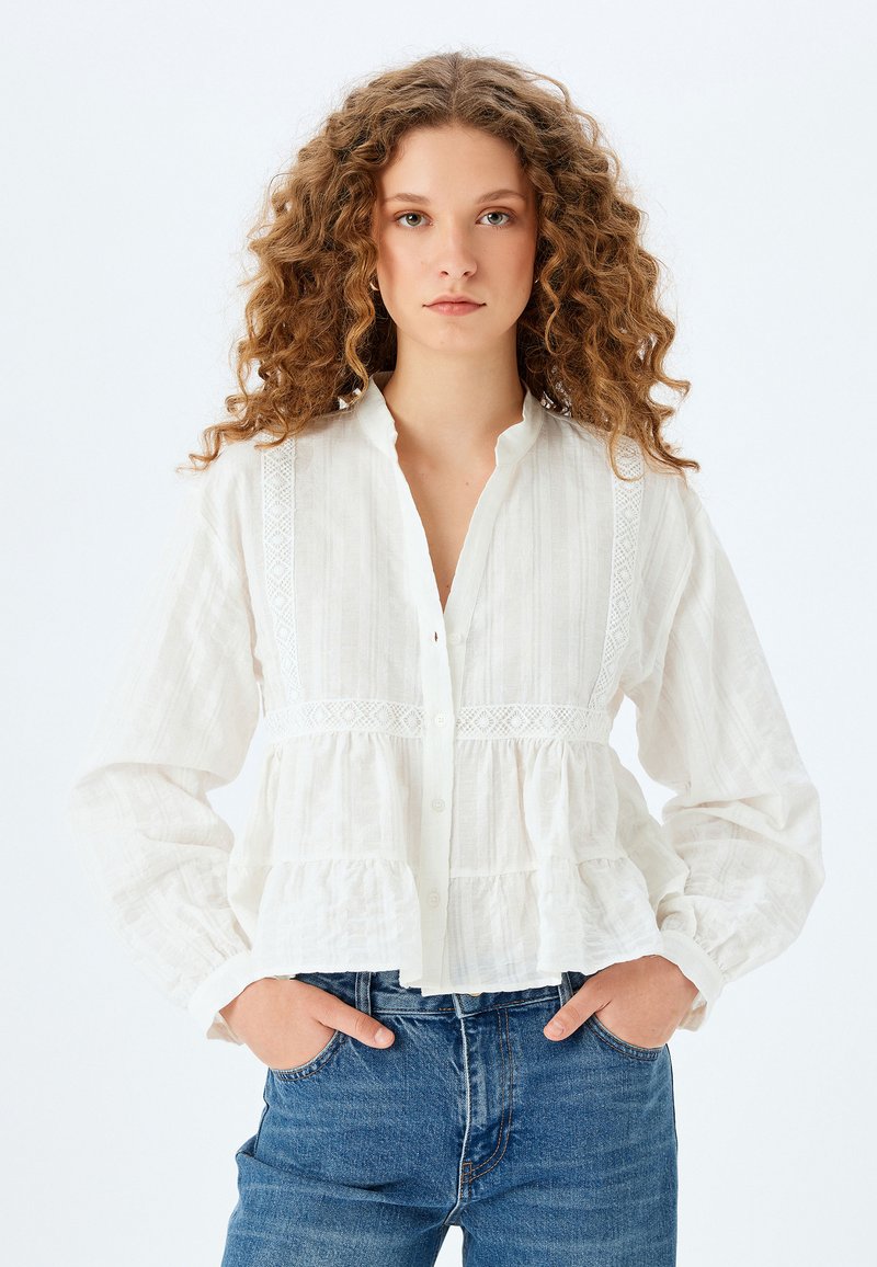 Witte blouse met knoopsluiting, van een gestructureerde stof, met kantdetails langs de schouders en een gathers peplum zoom. Gekocht met denim jeans.