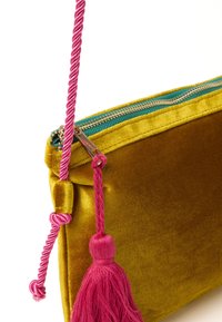 Busta gialla in velluto con una cerniera turchese, caratterizzata da una tracolla intrecciata rosa e un accento con un pon-pon rosa. Texture complessivamente liscia.