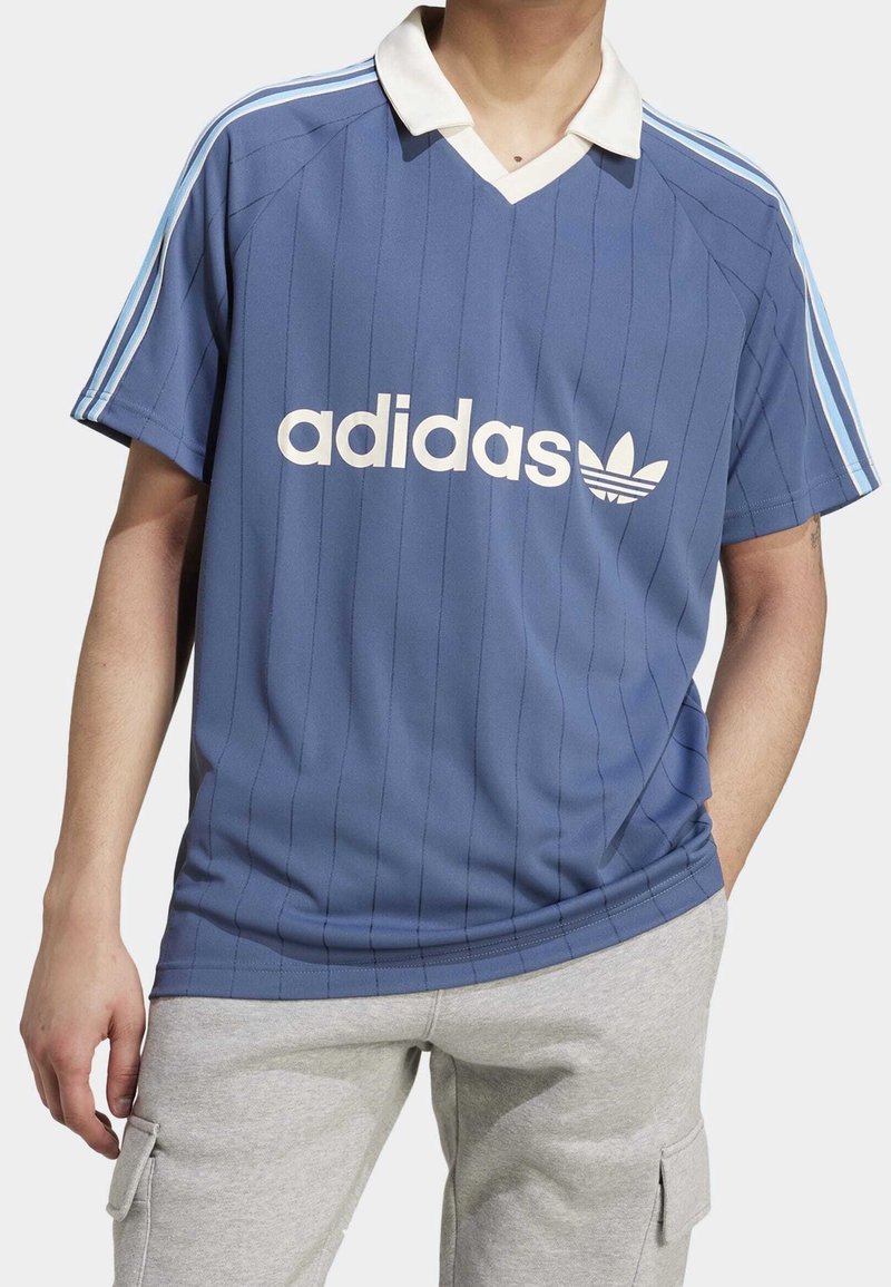Blå Adidas fotbollsjacka med randigt mönster, vit krage och stort vitt logo på framsidan, med tre vita axelränder.