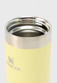 Θερμός από ανοξείδωτο ατσάλι με ματ παστέλ κίτρινο εξωτερικό, ασημένιο περιθώριο και λογότυπο. Κομψός κυλινδρικός σχεδιασμός με λεία υφή.