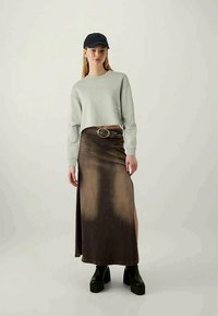 Light gray cropped sweatshirt paired with a long, dark brown denim skirt featuring a high side slit, accented with a round belt and chunky black shoes.