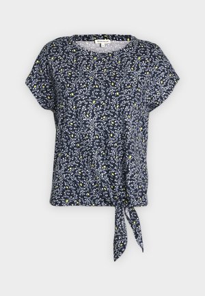 Donkerblauwe blouse met korte mouwen, wit bladmotief, gele stippen, ronde halslijn en een voorstrikdetail aan de zoom.