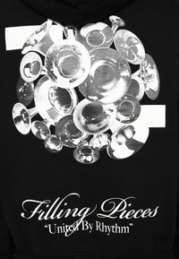 Ensemble d'instruments de musique en laiton brillant disposés en sphère au-dessus du texte : Filling Pieces « United By Rhythm » sur fond en tissu noir.
