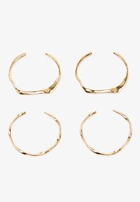 Quatre bracelets en métal doré avec un design ondulé et texturé. Chacun a une forme à extrémité ouverte, variant en taille et en courbure.
