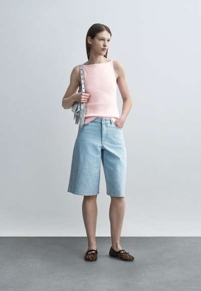 Γυναίκα με ροζ τοπ χωρίς μανίκια, ανοιχτό μπλε cropped παντελόνι φαρδιάς γραμμής, παπούτσια με λεοπάρ μοτίβο, κρατώντας μια γκρι τσάντα ώμου.