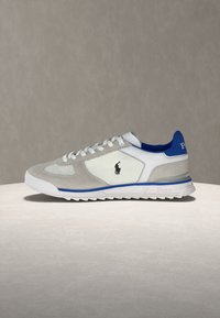 Λευκό και γκρι αθλητικό παπούτσι με μπλε λεπτομέρειες και μαύρο λογότυπο Polo στο πλάι, τοποθετημένο σε φωτεινή επιφάνεια με ουδέτερο φόντο.