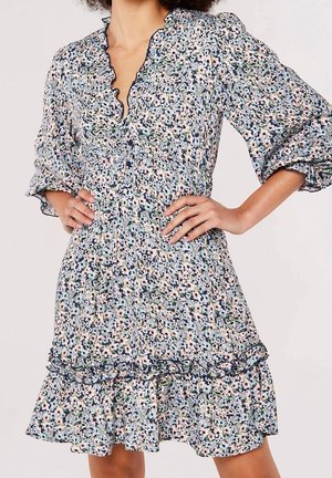 Vrouw die een bloemenjurk draagt met een geplooide halslijn, driekwart pofmouwen, een elastische taille en een uitlopende zoom met ruches.