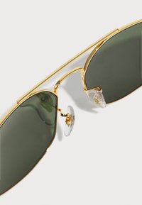 Gafas de sol de metal dorado con lentes verdes, con un marco delgado, almohadillas nasales transparentes y un diseño minimalista.