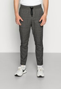 Grå ternede sweatpants med elastisk talje og snører, tapered fit, parret med hvide atletik sko med sorte accenter.