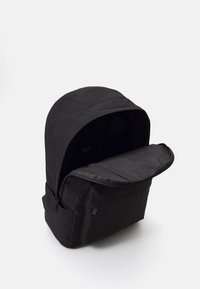 Črna nahrbtnik iz trpežnega blaga, z zaobljenim vrhom, velikim žepom na zadrgo in elegantnim, minimalističnim oblikovanjem.