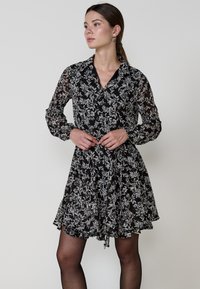 Rochie neagră cu imprimeu floral, cu guler, mâneci lungi și talie strânsă. Material moale cu modele florale albe. Poale care curg.