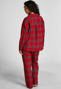 Rode geruite pyjama set met een knoopsluiting shirt en bijpassende broek, gemaakt van zachte stof met een relaxte pasvorm en een patchzakdetail.