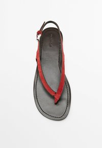 Rote Wildleder-Zehentrenner mit flacher schwarzer Ledersohle, verstellbarem Riemen und gestickten Details.