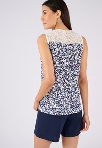 Mouwloze blouse met een marineblauwe, roze en crèmekleurige bloemenpatroon, met een kanten paneel op de schouders en een soepele, lichte stof.