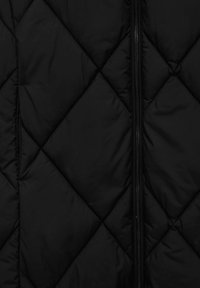 Tissu matelassé noir avec coutures en losange et une fermeture éclair noire verticale au centre.