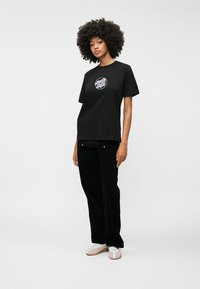 Μαύρη βαμβακερή μπλούζα με κοντά μανίκια και στρογγυλή λαιμόκοψη, με κυκλικό γραφικό σχέδιο σε λευκό και μωβ στο στήθος.