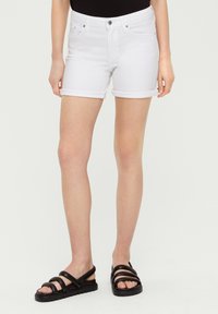 Witte denimshorts met opgerolde ommouwen en voorzakken. In combinatie met zwarte sandalen met bandjes en een gestructureerde zool. Eenvoudig ontwerp zonder patronen.