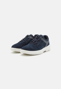Tenisi din suede de culoare bleumarin, cu talpă din cauciuc alb, având șireturi și un superior texturat, plus un toc mic pentru un confort sporit.