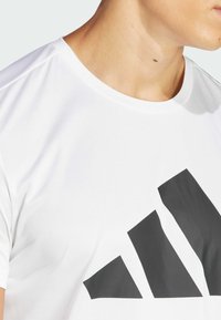 Camiseta atlética de manga corta blanca con un gran logo triangular negro en la parte frontal. Textura suave y cuello redondo.