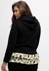 Felpa nera con cappuccio e orlo arricciato stampato floreale che presenta tonalità di verde e rosa. Tessuto morbido e design aderente.