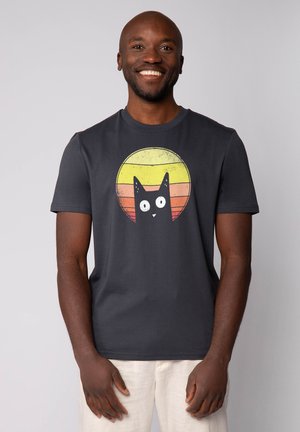 Dark gray cotton t-shirt featuring a cartoon black cat with wide eyes, set against a circular yellow and orange gradient background.