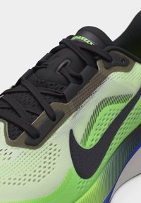 Κοντινό πλάνο ενός αθλητικού παπουτσιού Nike σε νέον πράσινο και μαύρο, με μαύρα κορδόνια και αεριζόμενη υφασμάτινη επιφάνεια.