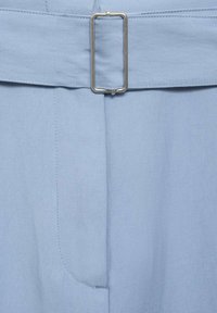 Helle blaue Stoffhosen mit einem breiten Gürtel und einer rechteckigen silbernen Schnalle sowie Fronttaschendetails, gefertigt aus einem glatten, strukturierten Material.