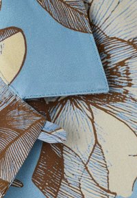 Modro blago z rožnim vzorcem v rjavi in krem barvi; vsebuje ostri robovi, gladko teksturo in prekrivajoče se dele.