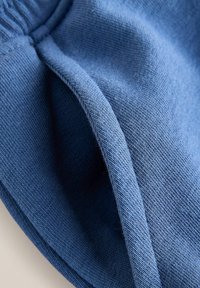 Gros plan sur un tissu tricoté bleu montrant la texture détaillée et les points de couture sur un matériau doux et plié.