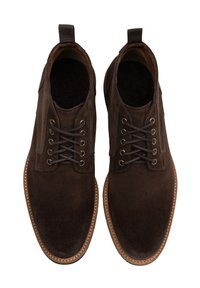 Botas de tobillo de ante marrón con puntera redonda, diseño con cordones y detalles en piel marrón. La vista superior muestra los agujeros para los cordones y una pequeña lengüeta.