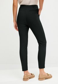 Slim-fit černé kalhoty s hladkou texturou, obsahující zadní kapsu a středně vysoký pas. Stylizováno se světlými hnědými nazouvacími botami.
