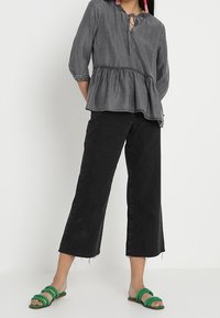 Šedý peplum top s tříčtvrtinovými rukávy, kombinovaný s černými širokými džíny a zelenými nazouvacími sandály. Mezi výrazné detaily patří výstřih s klíčovou dírou.